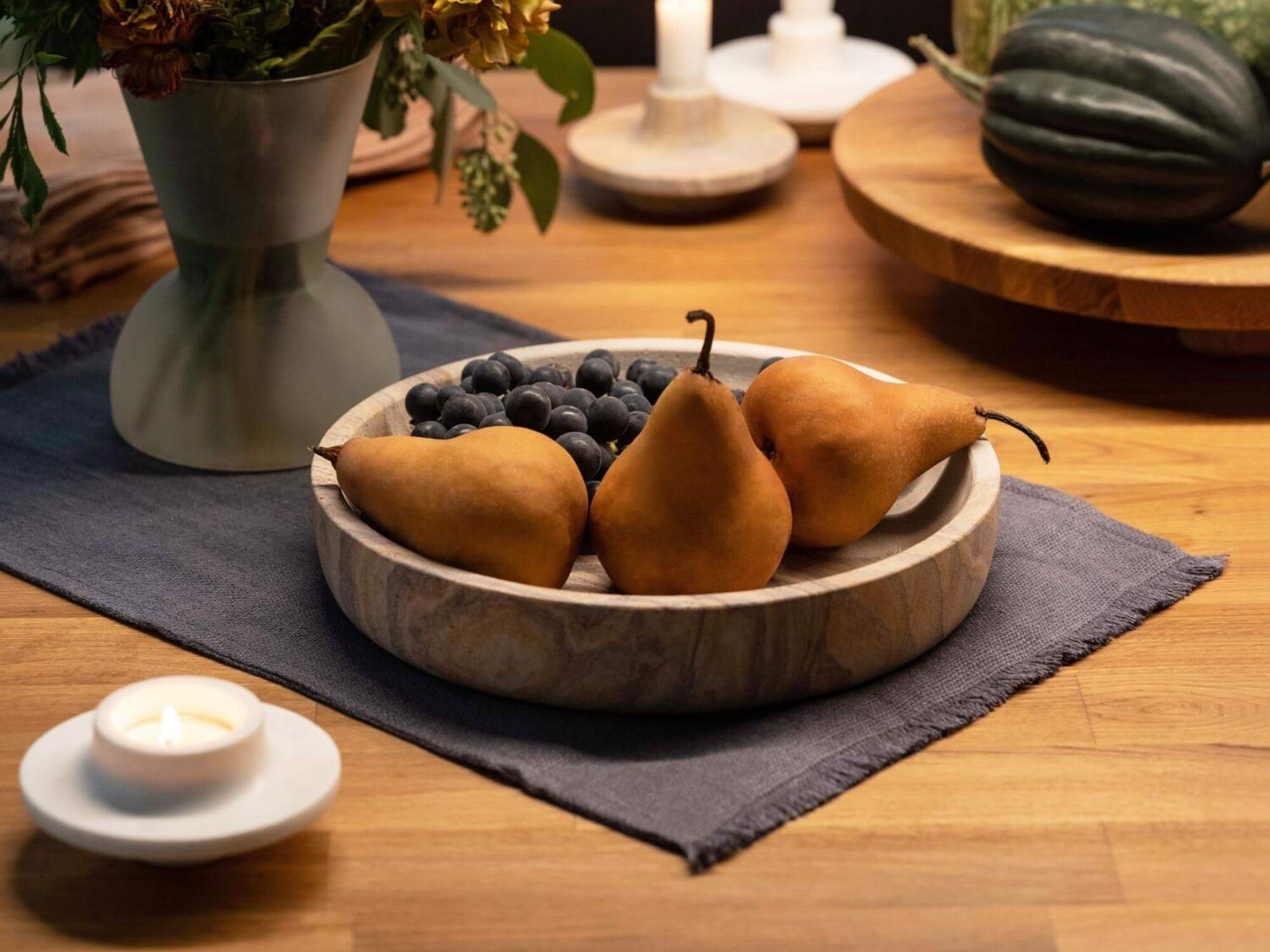 Grey placemat with vase, display bowl, candles, and wood tray on table